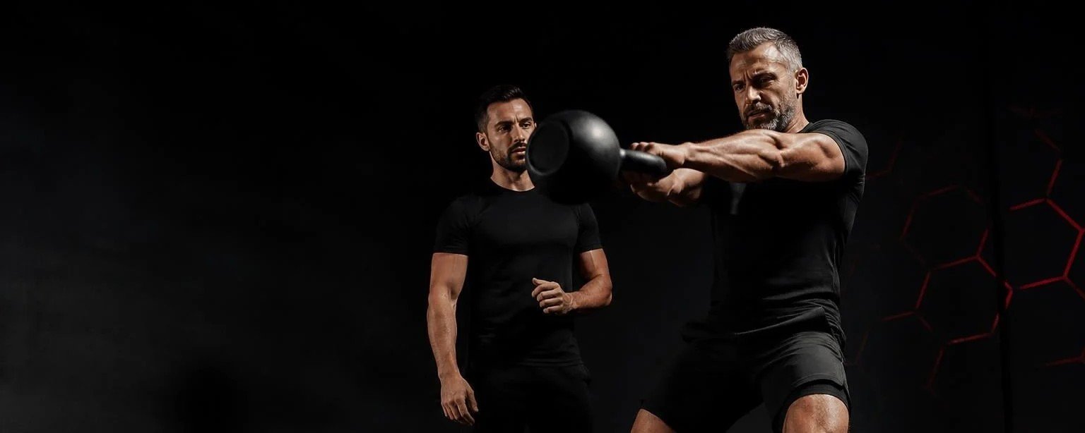 Entraînement et graisse viscérale après 40 ans Homme de 47 ans réalisant un kettlebell swing sous le regard de son coach en séance individuelle